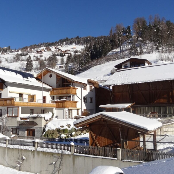The Farm House exterior features white facades and wooden balconies, surrounded by snow-covered hills and additional farm buildings in a winter setting.