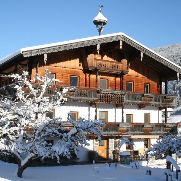 Der Bauernhof im Winter mit traditioneller Holzarchitektur, Balkonen und verschneiter Umgebung.