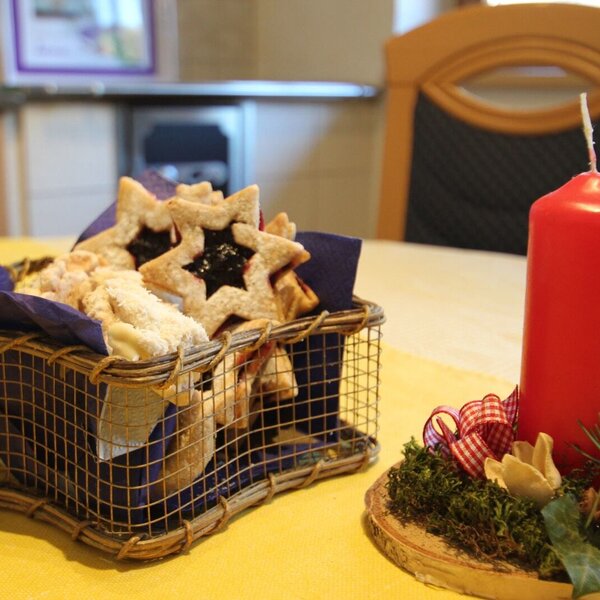 Ein Korb mit Gebäck und eine rote Kerze auf einem dekorierten Holzsockel auf dem Tisch im Bauernhof.