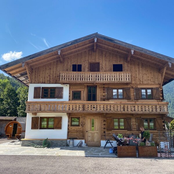 Das Bauernhofgebäude mit Holzbalkonen, Fenstern mit Holzläden, umgeben von Bergen.