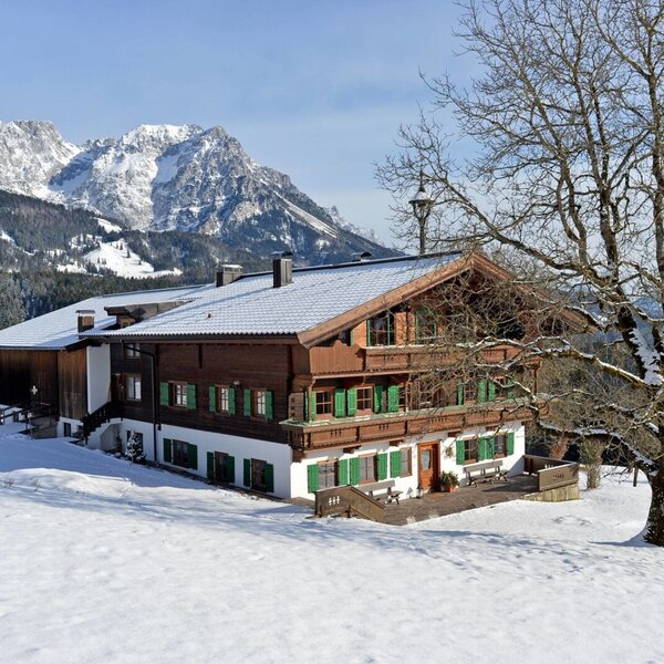 The Farmhouse exterior with its wooden facade, green shutters, and balconies, set against snow-covered mountains.