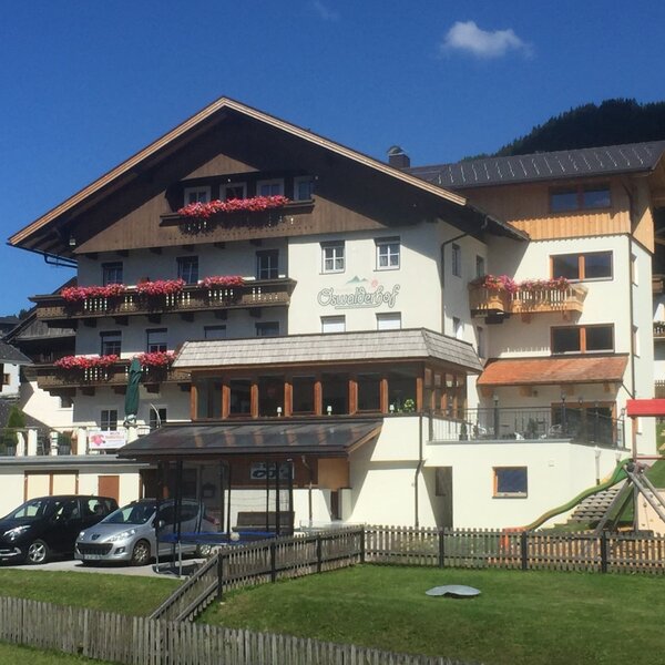 Der Bauernhof Schauflerhof von außen, mit Balkonen, Parkplätzen und einem Kinderspielplatz im Garten.
