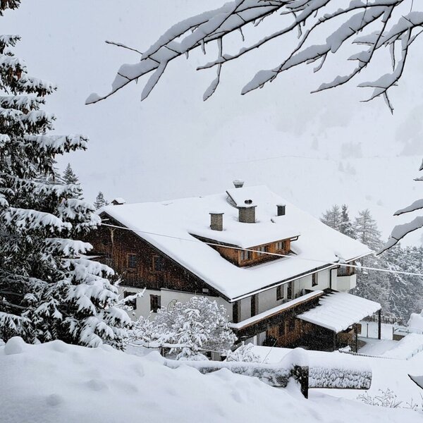 Der Bauernhof im Winter, umgeben von schneebedeckten Bäumen und einer winterlichen Landschaft.