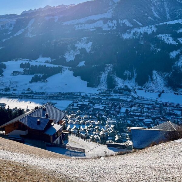 Blick vom Bauernhof auf die schneebedeckte Berglandschaft und das Tal mit dem Dorf.