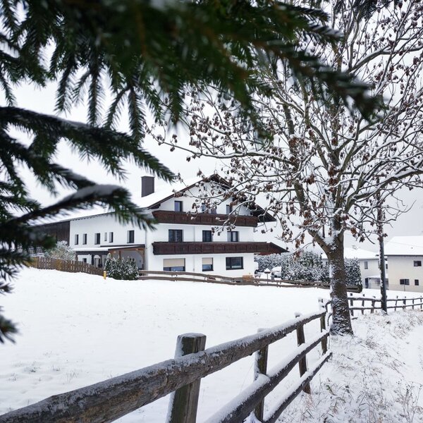Exterior view of the farmhouse in winter, with a snow-covered landscape and a wooden fence.