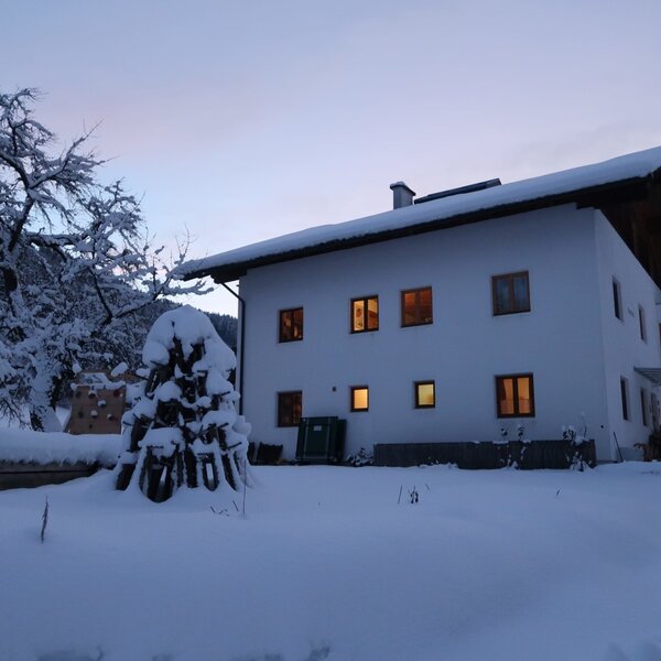 Der Bauernhof im Winter, umgeben von Schnee und mit beleuchteten Fenstern.
