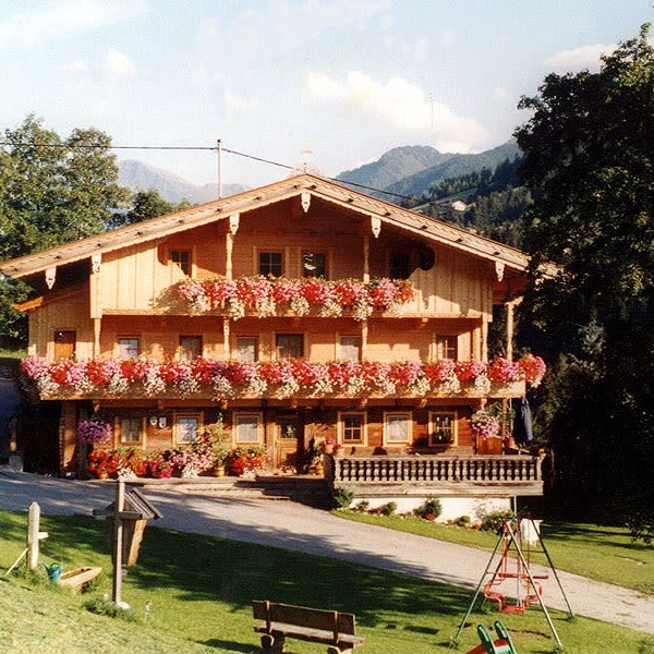 The Farm House, with its wooden exterior and balconies adorned with flowers, offers a garden area with a children's swing set and mountain views.