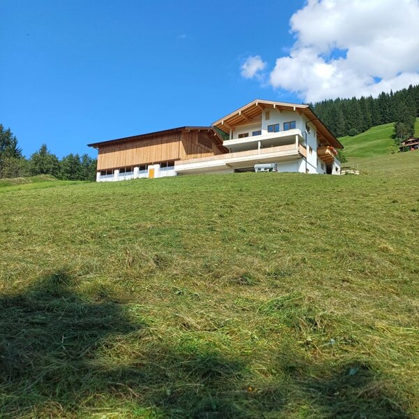 Der Bauernhof mit modernem Wohnteil und angrenzendem Wirtschaftsgebäude, gelegen auf einer grünen Wiese am Hang.