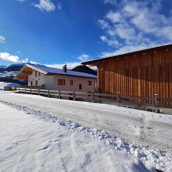 The farmhouse in winter, with a snow-covered access road and a wooden outbuilding.