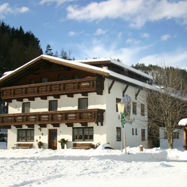 Der winterliche Bauernhof mit charakteristischen Holzbalkonen, umgeben von Schnee und Wald.