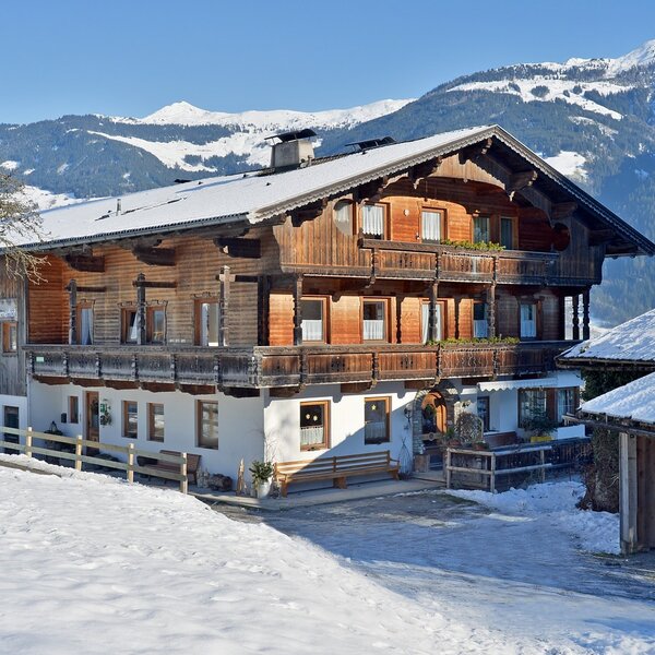 Außenansicht des Bauernhofs mit traditioneller Holzfassade und Balkonen, umgeben von Schnee und Bergen.