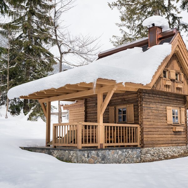 Die Alm im verschneiten Wald, mit einer Veranda und Holzbalken.