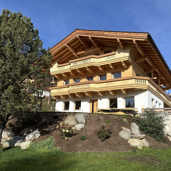 Außenansicht des Bauernhofs mit traditionellen Holzbalkonen und einer Fassade aus Holz und Weißputz.