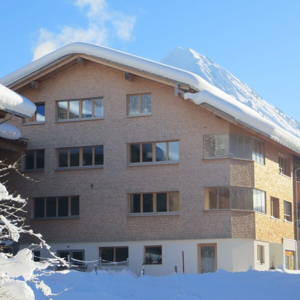 Außenansicht des Bauernhofs mit Holzfassade, schneebedecktem Dach und Balkonen, der die Ferienwohnungen in winterlicher Umgebung beherbergt.