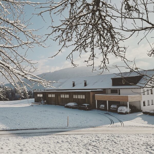 The Farm House in winter, surrounded by a snow-covered landscape with a covered parking area for guests.