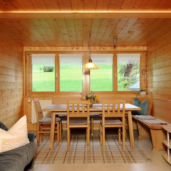 Die geräumige Wohnküche der Ferienwohnung im Bauernhof, komplett mit massiven Holzmöbeln vom Tischler und einer Sitzbank, bietet Aussicht auf die umliegenden Wiesen.