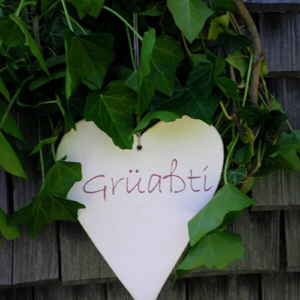 A heart-shaped sign displaying 'Grüaßti' (a local greeting) is surrounded by ivy on the exterior wall of the Farm House.