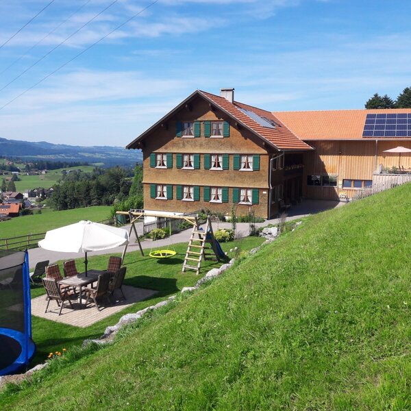 Der Bauernhof mit Außenterrasse, Spielbereich inklusive Trampolin und Schaukel sowie Bergblick.