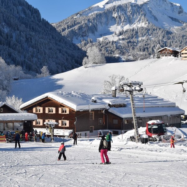 Die Skipiste mit Skilift direkt vor dem Bauernhof, umgeben von schneebedeckten Bergen.
