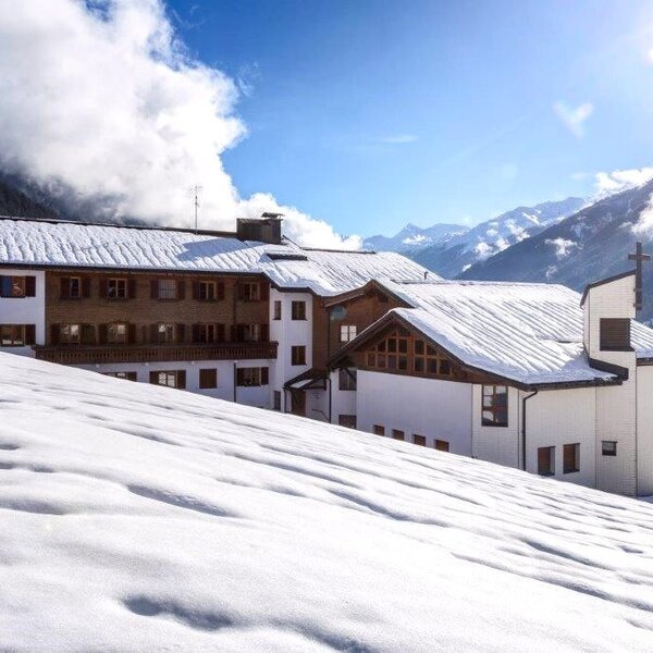 Der verschneite Bauernhof mit angrenzender Kapelle und Bergpanorama.