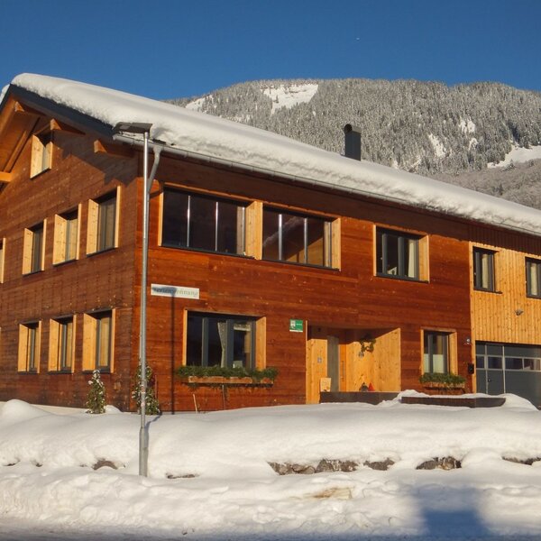 The solid wood Farm House, newly built in 2022, seen covered in snow during winter with mountain views.